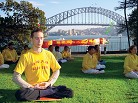 Published on 1/7/2002 Falun Gong practitioners in yellow T-shirts practice Exercise Five in a park. (Note: If anyone can identify the bridge in the background we can give the location)