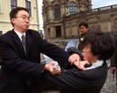 2002年4月11日，江泽民访德时，为阻止学员喊‘法轮大法好’，中国保安公开掐住女学员脖子